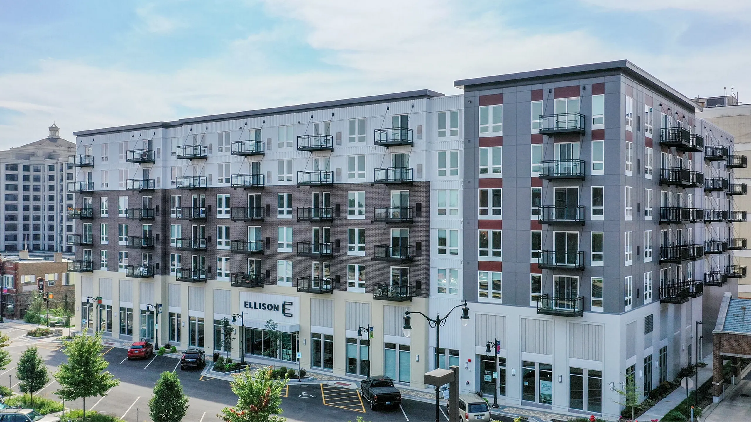 Modern urban apartment building with sleek architecture, featuring multiple balconies and large windows, set against a vibrant cityscape.