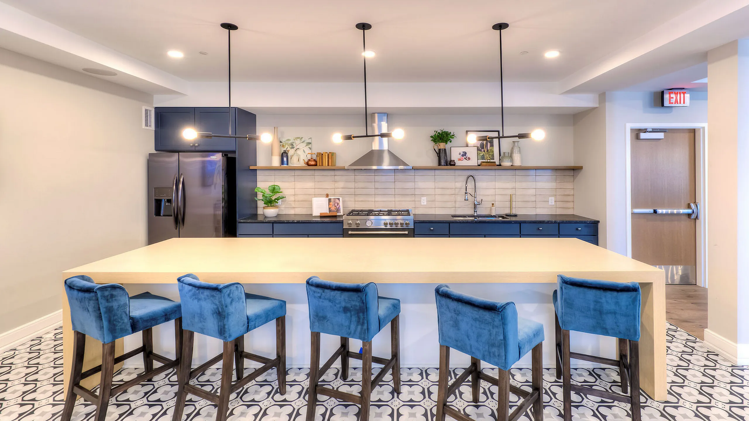 Modern kitchen with sleek cabinetry, elegant lighting, and vibrant blue velvet barstools, creating a stylish and inviting space.
