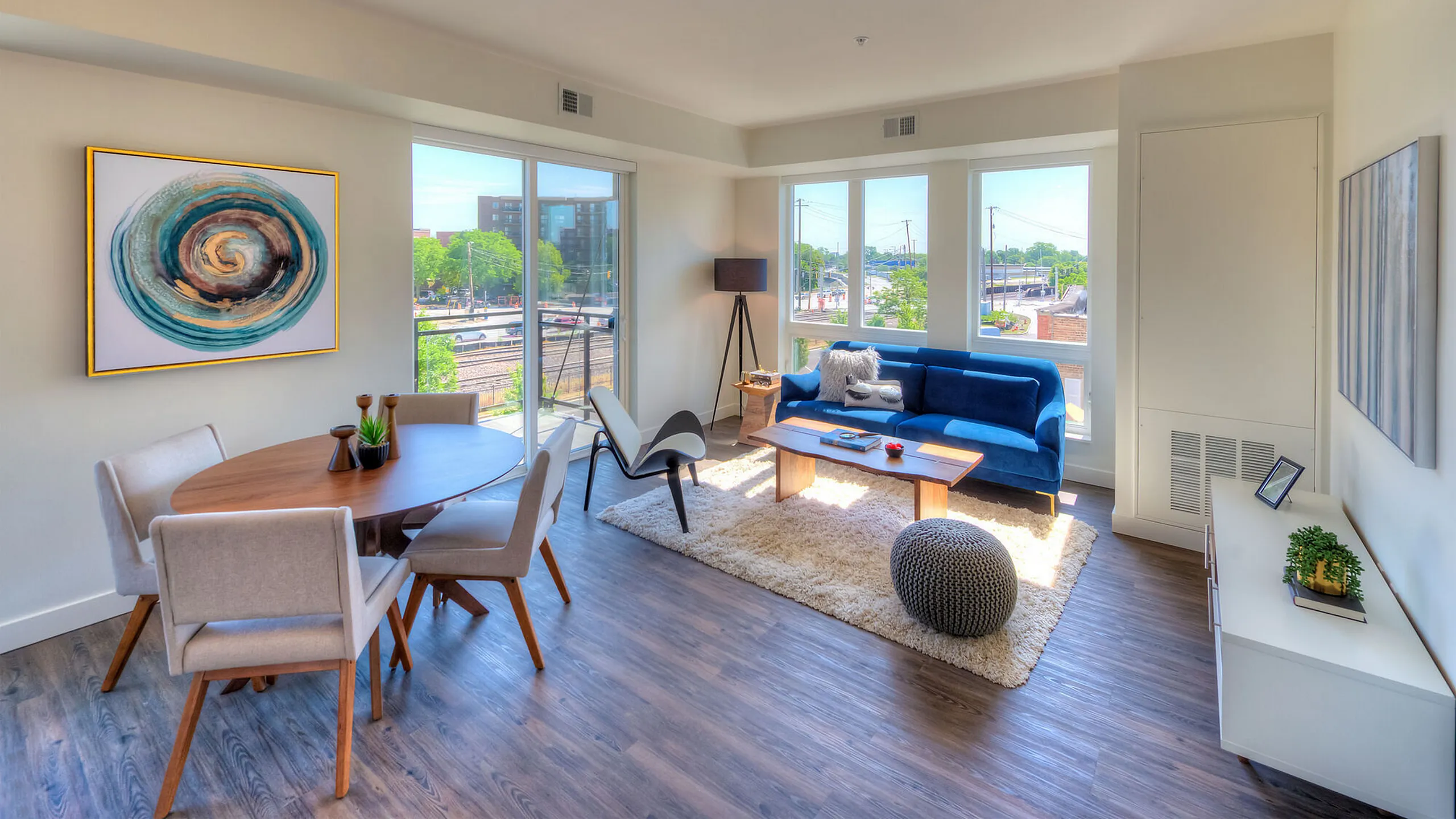 Bright and modern open-plan living room with a plush blue sofa, chic dining area, and large windows providing abundant natural light.