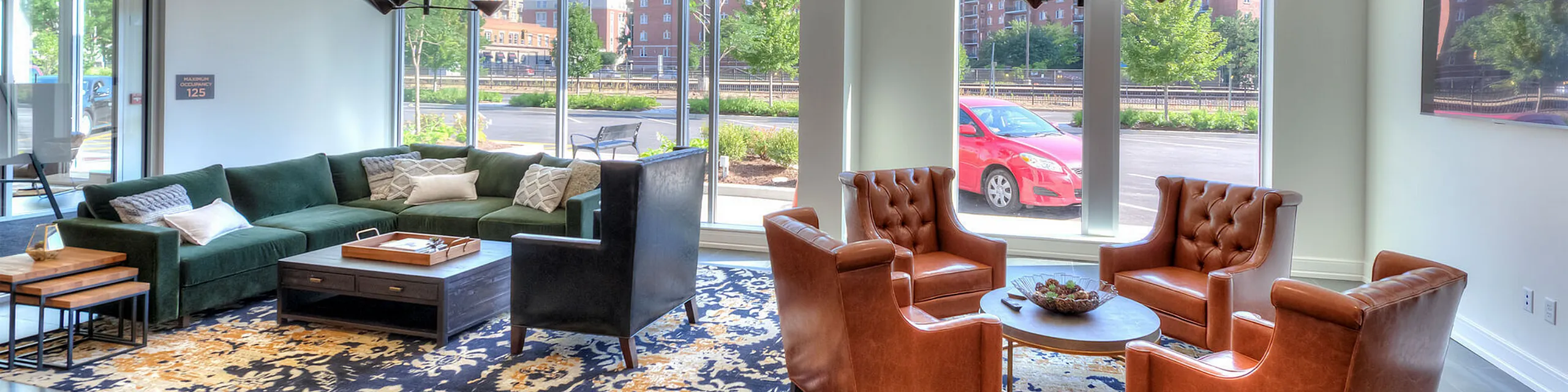 Bright and modern living room with large windows, elegant leather chairs, and a plush green sofa, perfect for relaxation and entertaining.
