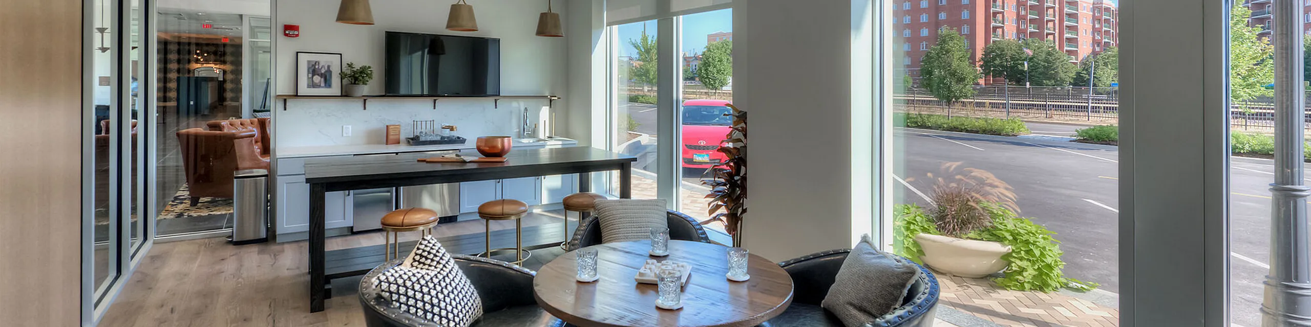 Bright and modern apartment lounge featuring a sleek kitchen island, stylish bar stools, and large windows offering a stunning city view.