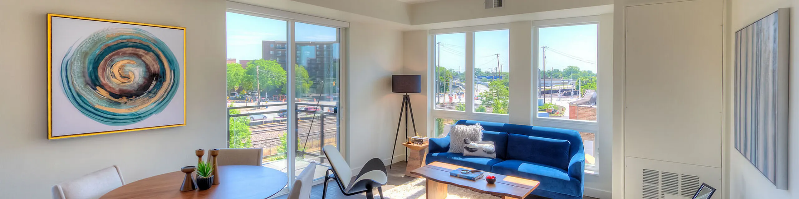Modern apartment living room with large windows, chic blue couch, stylish decor, and bright, natural light.