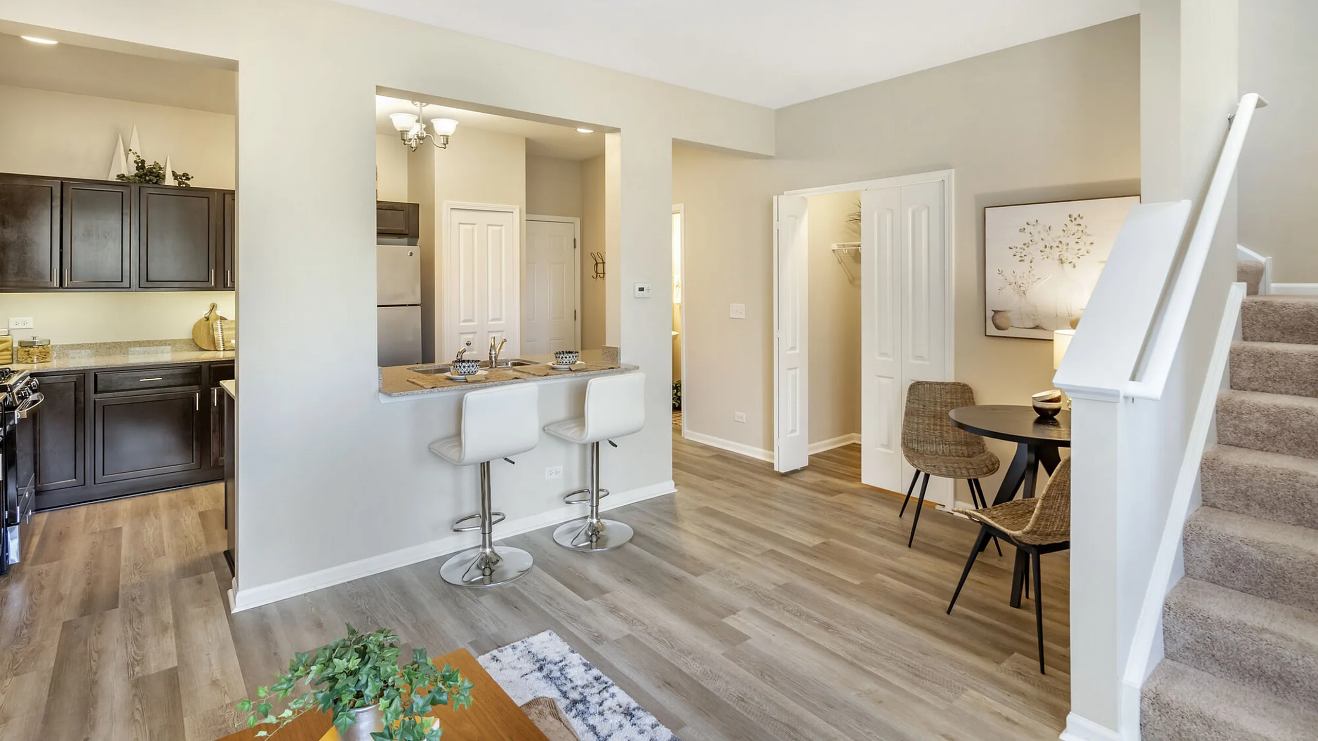 Modern apartment interior with open kitchen, cozy breakfast bar, and elegant dining area beside carpeted stairs.