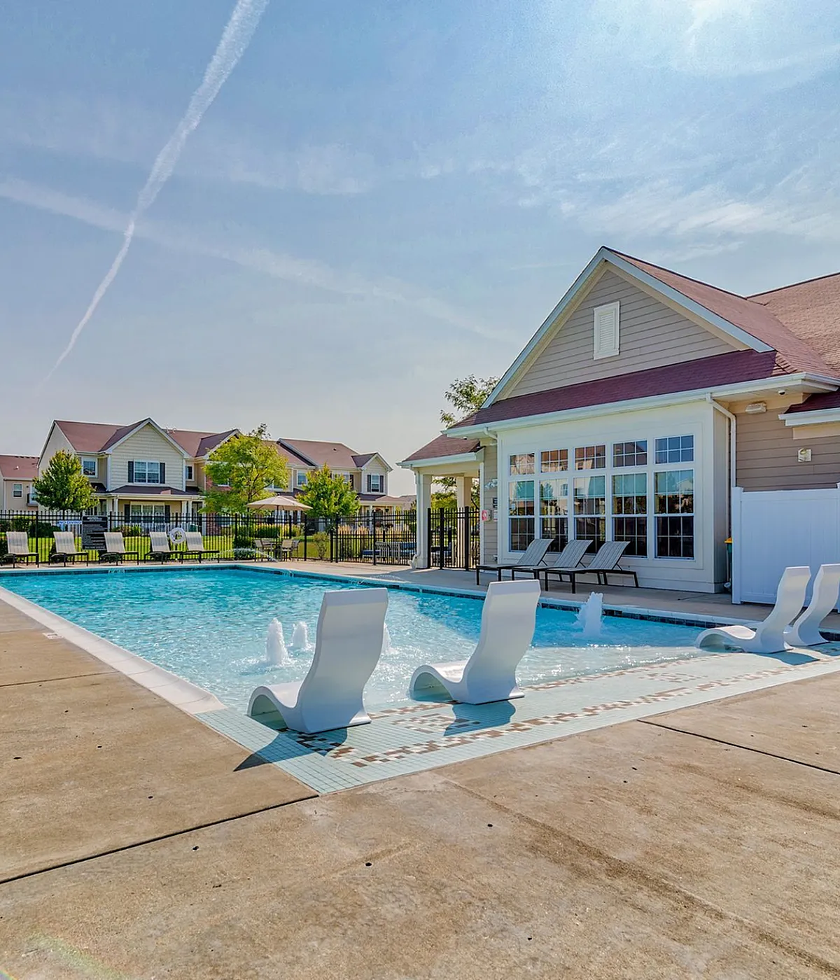 Inviting community pool area with ample sun loungers and a charming clubhouse, perfect for relaxation and social gatherings under a clear blue sky.