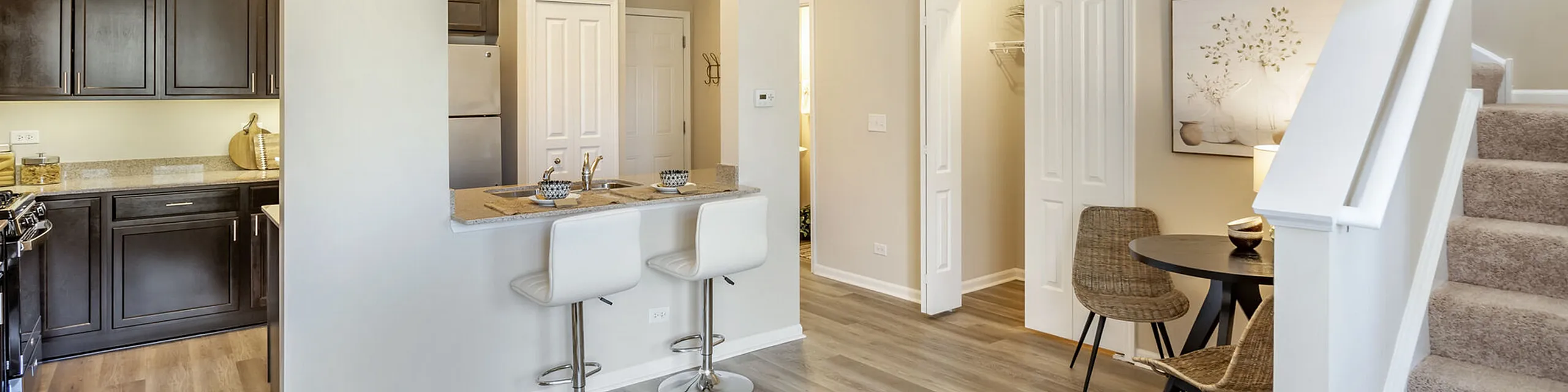 Charming open-concept apartment with a cozy breakfast bar, sleek kitchen cabinetry, and inviting dining area next to a well-lit staircase.