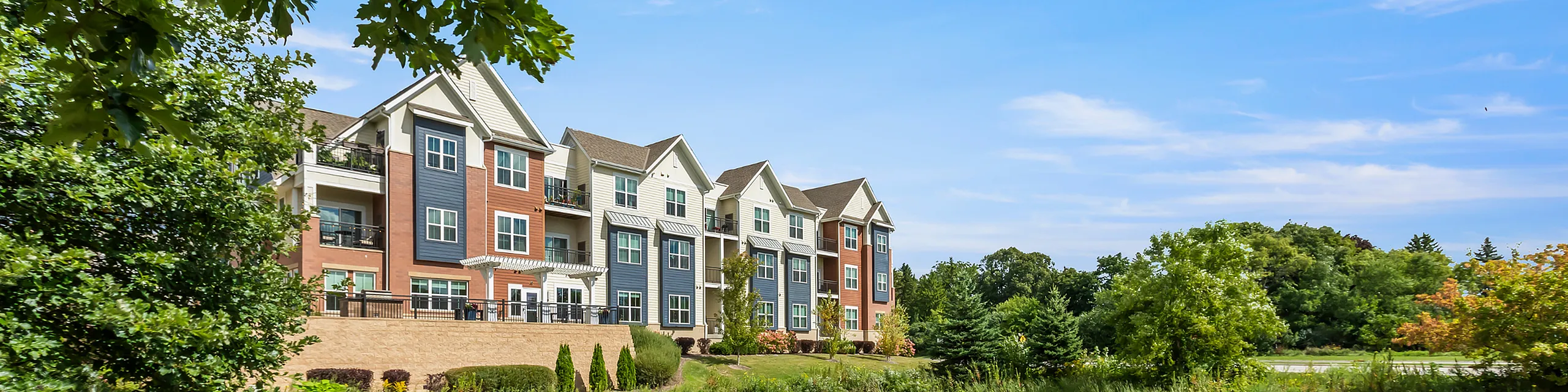Charming apartment complex exterior featuring contemporary design, surrounded by lush greenery and a clear blue sky.