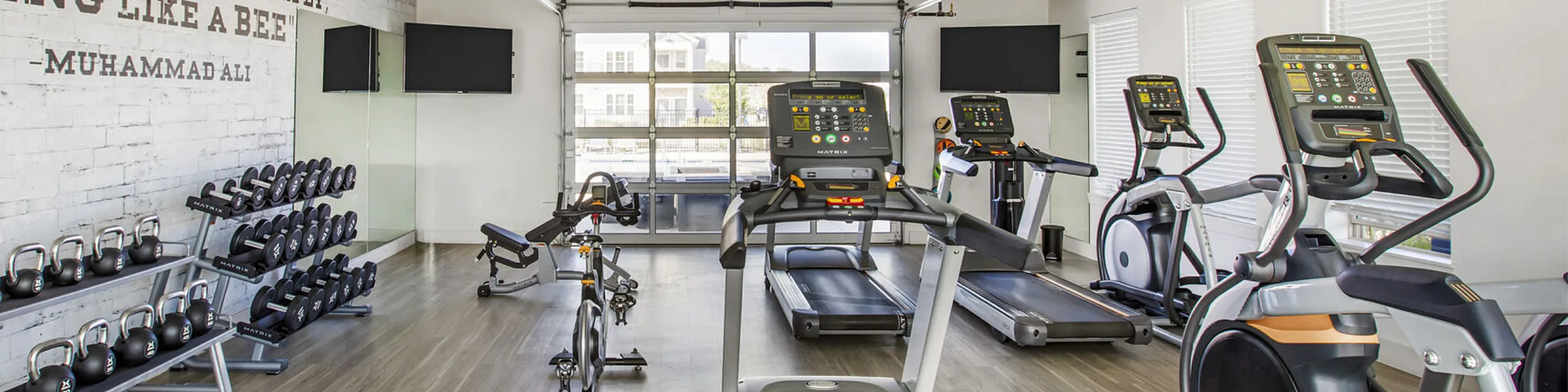 Modern apartment gym boasting state-of-the-art equipment, large windows, and motivational quotes on the wall for an inspiring workout environment.