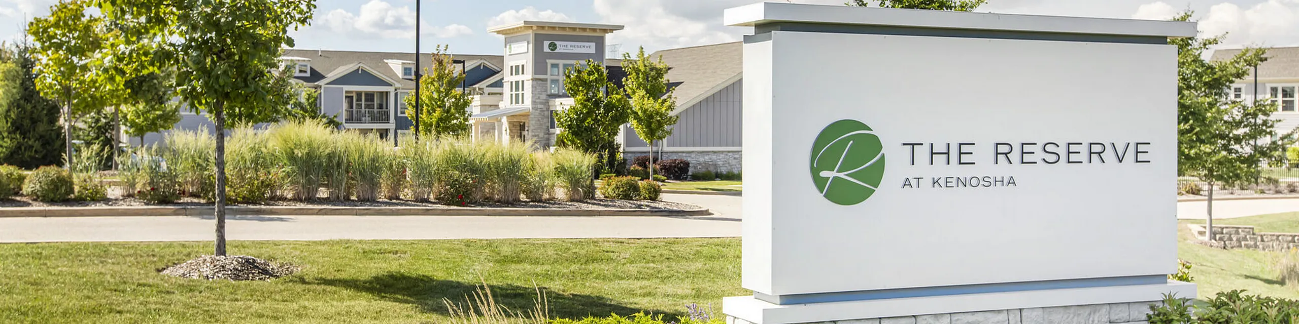 Inviting entrance of The Reserve at Kenosha with manicured landscapes and modern architecture under a bright sky.