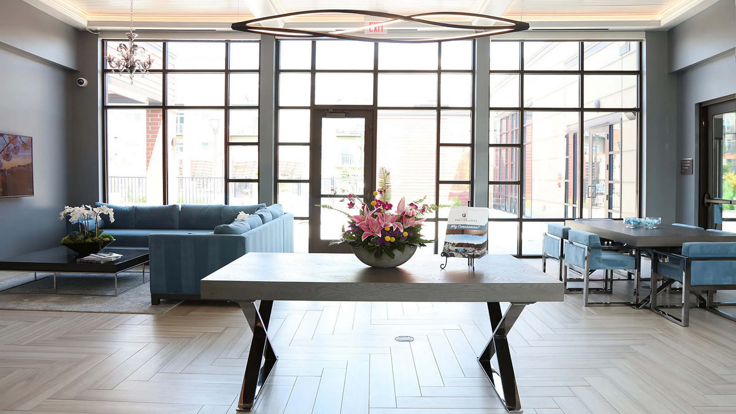 Bright and elegant living area with expansive windows, modern chandelier, plush blue seating, and a sleek dining table, perfect for entertaining and relaxation.