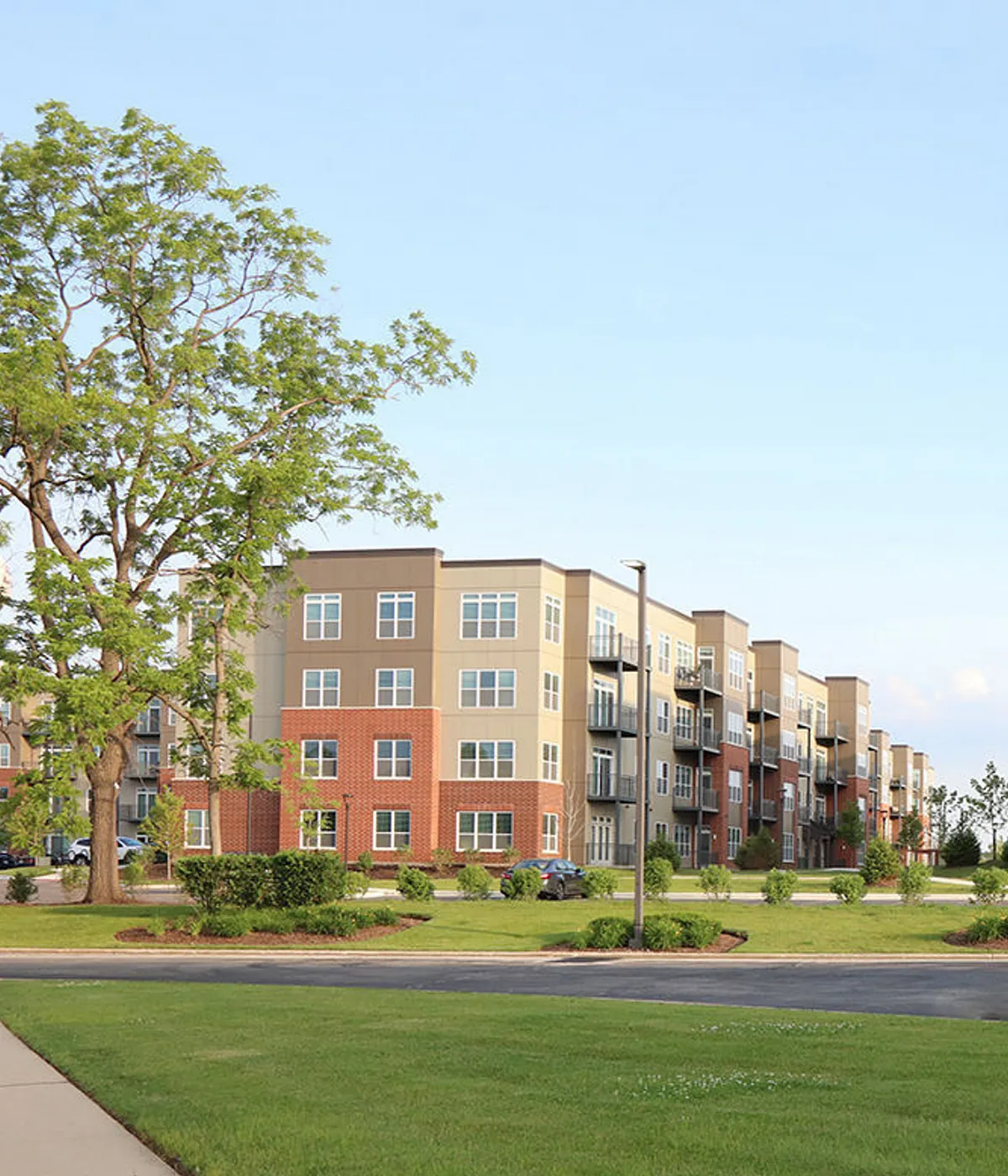 Modern apartment complex with lush green surroundings, featuring elegant architecture and multiple balconies.