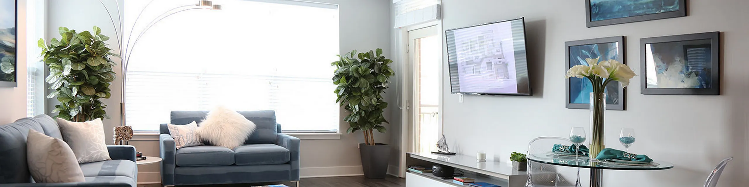 Contemporary living room with stylish gray sofas, lush green plants, and elegant decor, featuring a wall-mounted TV and modern art.