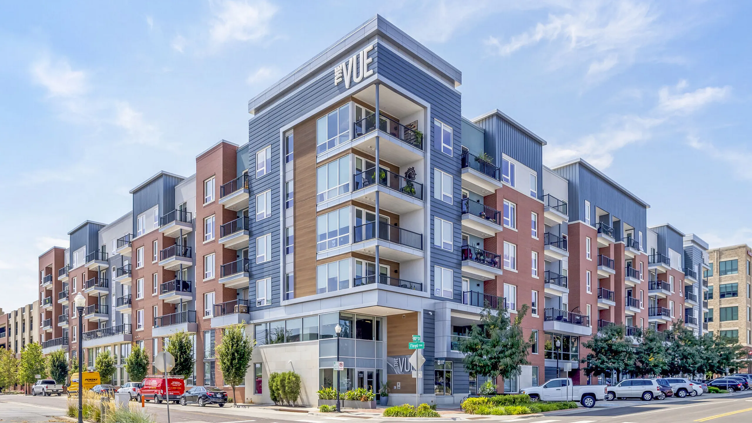 Modern apartment complex with expansive balconies, stylish facade, and vibrant urban surroundings on a sunny day.