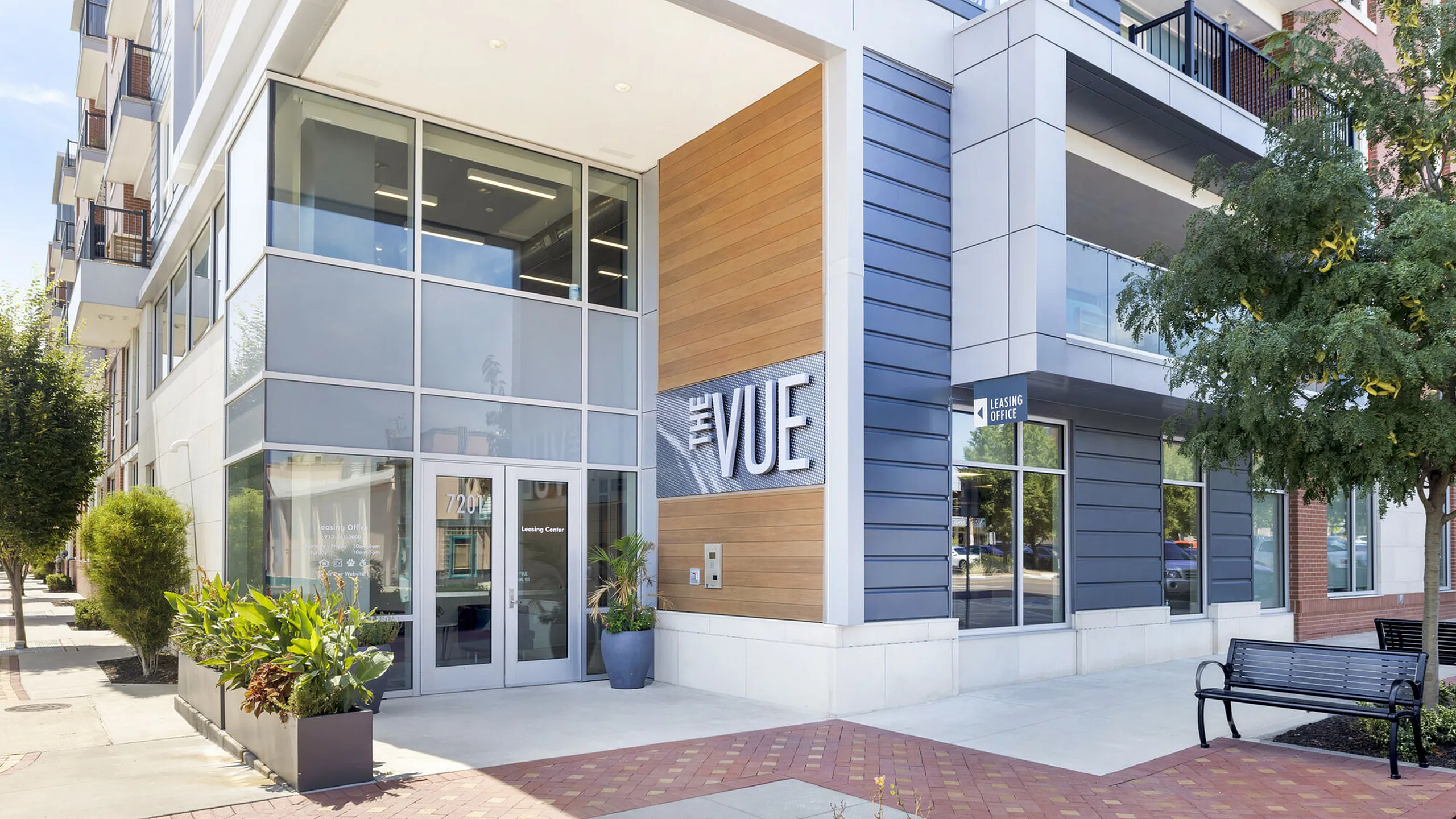 Modern apartment exterior featuring 'The Vue' leasing office with sleek glass and wood design, lush greenery, and inviting entrance.