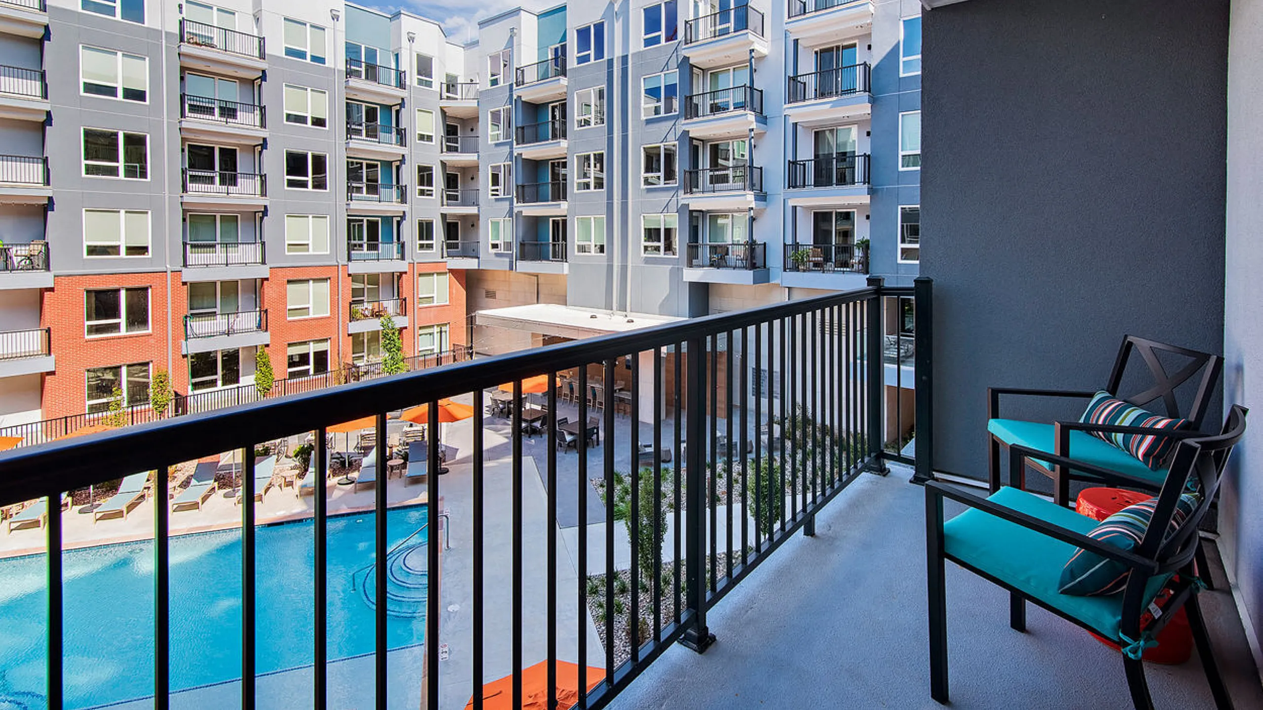 Chic apartment balcony offering a stunning poolside view with stylish outdoor seating and modern apartment complex backdrop.