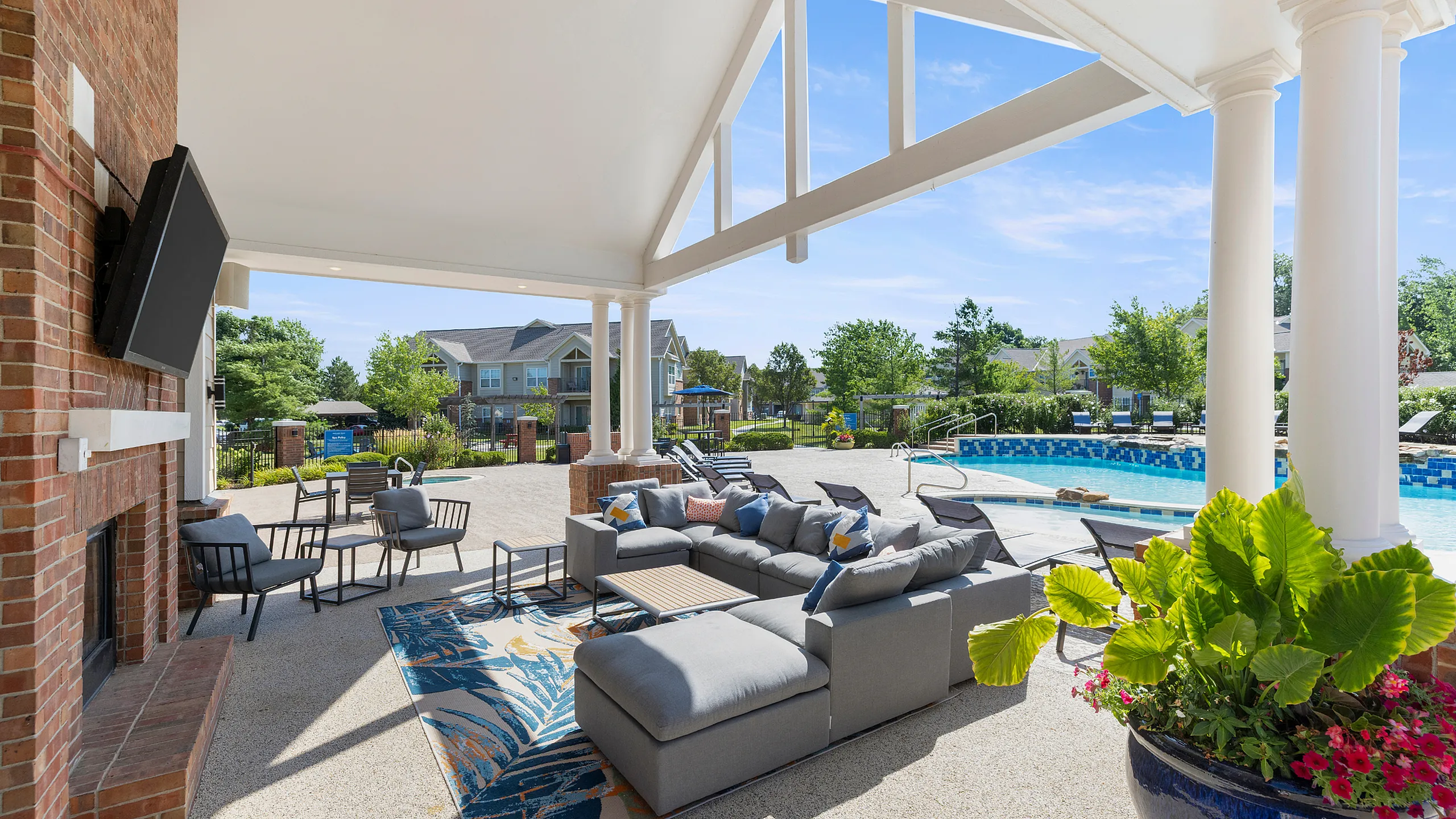 Luxurious outdoor lounge area with cozy seating overlooking a sparkling pool, set against a backdrop of lush greenery and modern architecture.