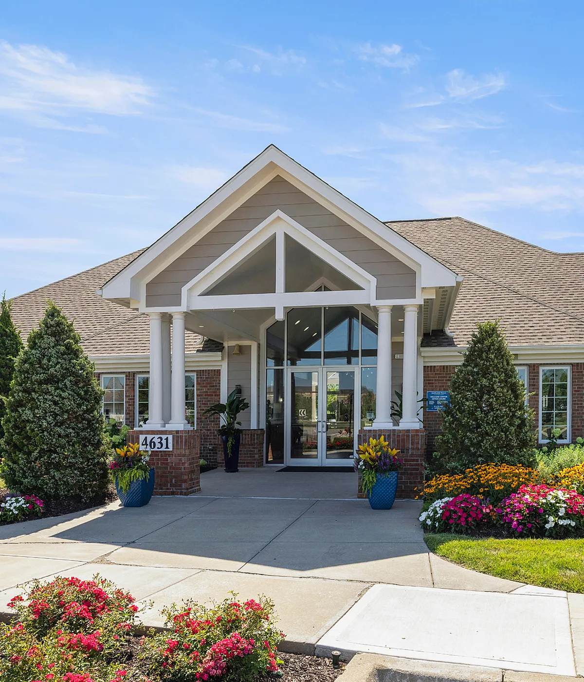 Elegant apartment entrance with lush landscaping and modern architecture under a clear blue sky.