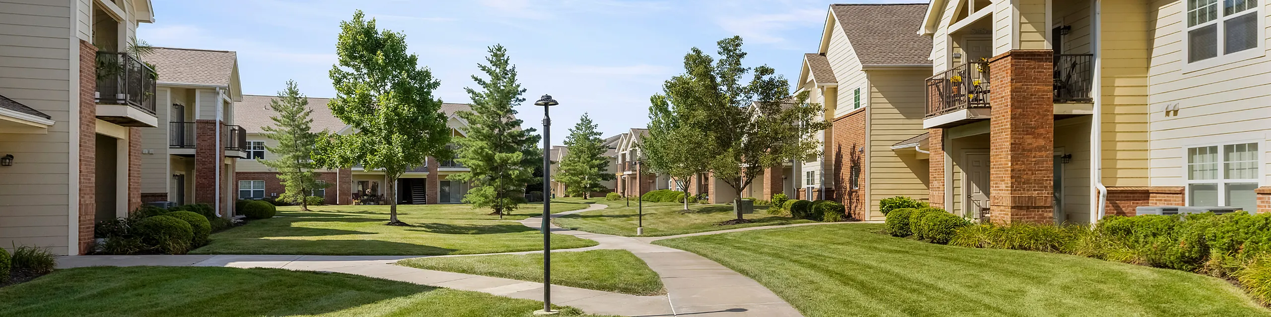 Charming apartment community with lush green lawns, mature trees, and cozy balconies.