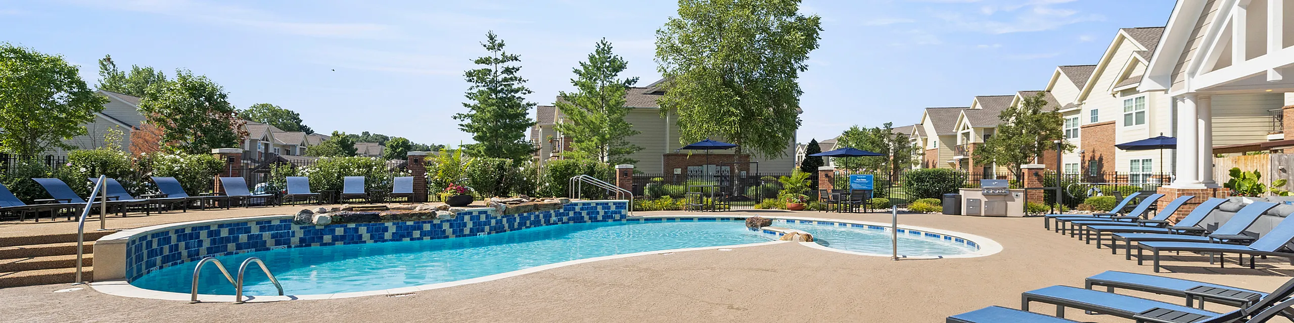 Inviting outdoor pool area with sleek lounge chairs and lush greenery, set against stylish apartment buildings.