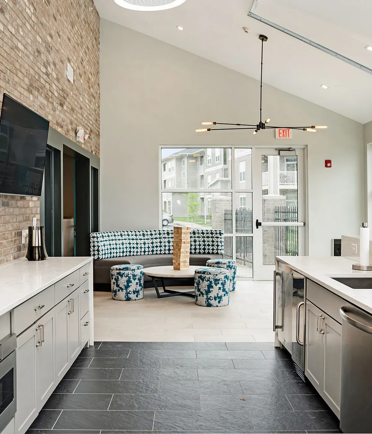 Modern apartment clubhouse featuring elegant open kitchen with sleek cabinetry, cozy seating area, and contemporary lighting design.