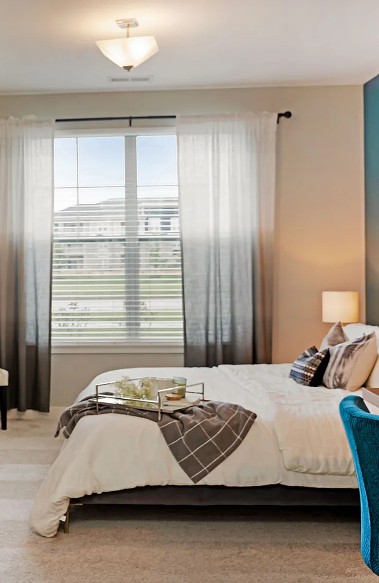 Inviting bedroom with cozy bedding, elegant lamps, and a large window offering natural light and neighborhood views.