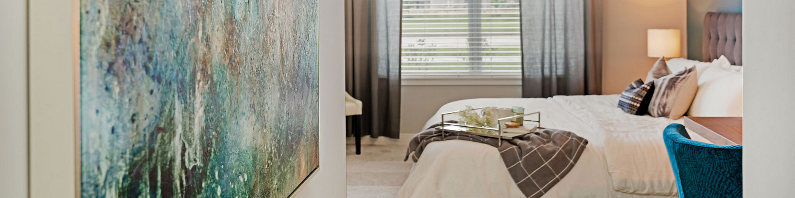 Inviting bedroom with elegant decor, featuring a plush bed, abstract wall art, and ample natural light through large windows.