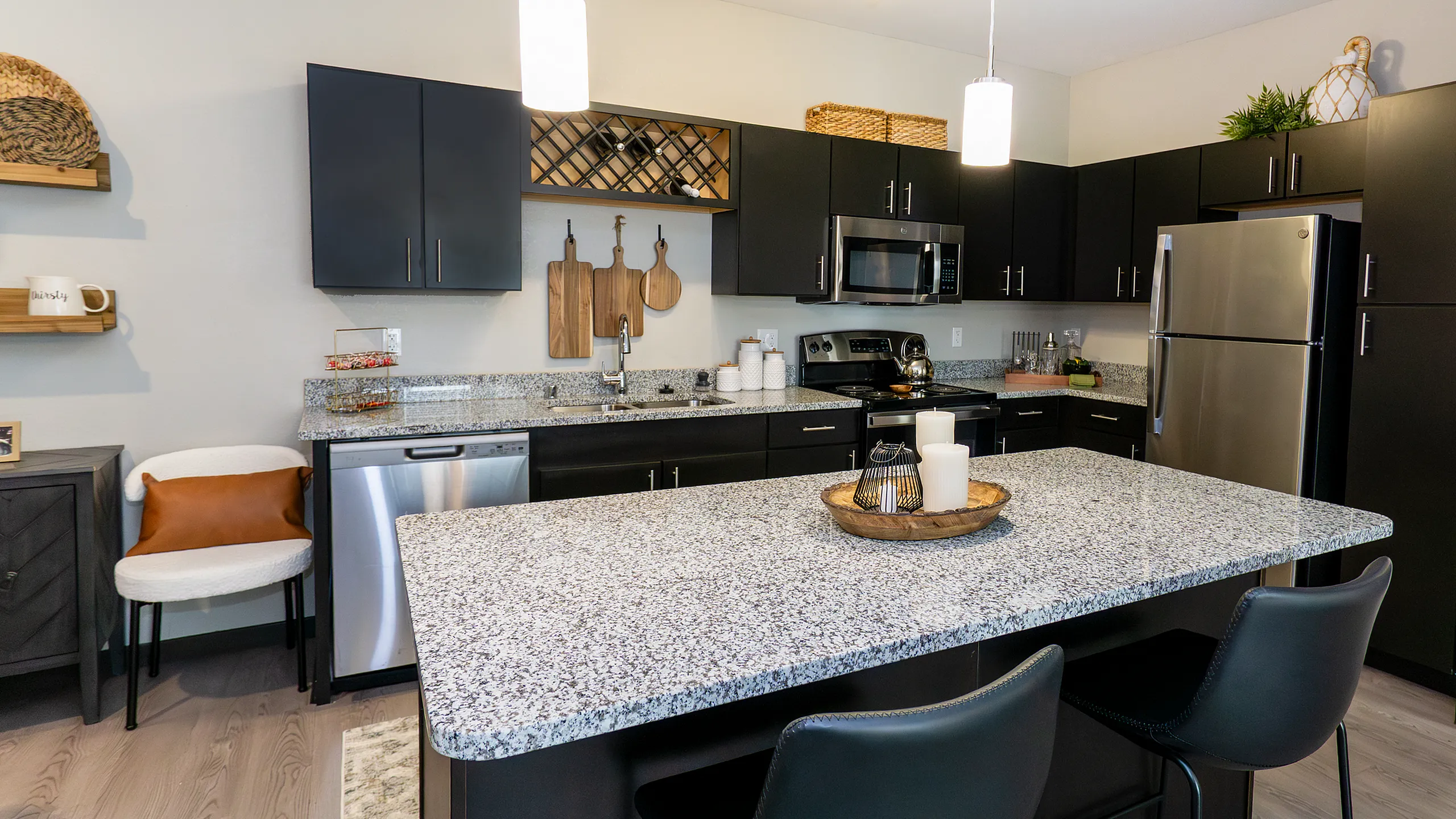 Modern kitchen with granite countertops, stainless steel appliances, and stylish dark cabinetry. Inviting island seating under elegant pendant lighting.
