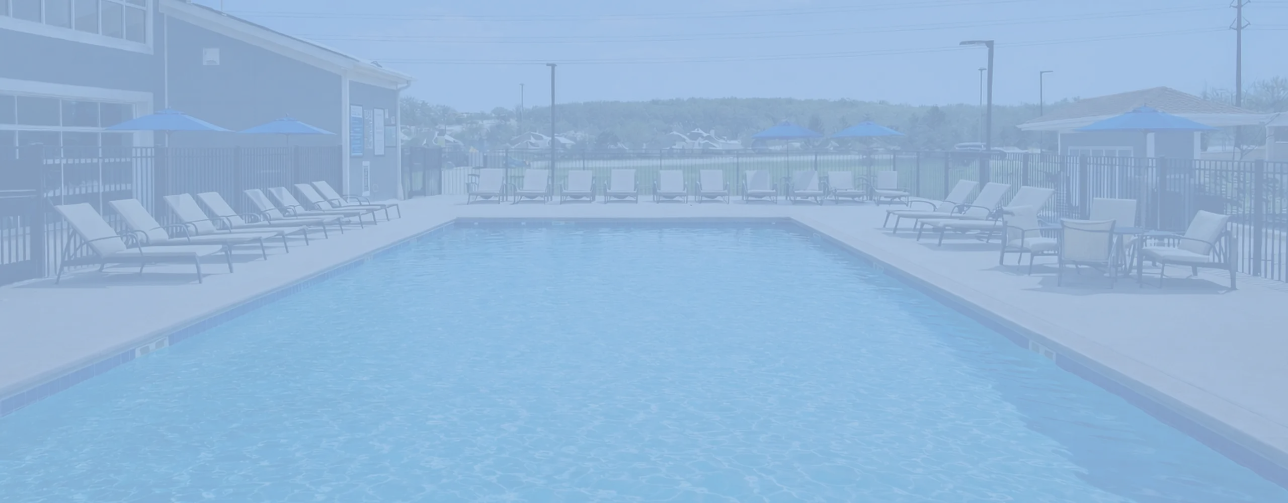 Inviting outdoor pool area with comfortable lounge chairs and blue umbrellas, perfect for relaxation and enjoying sunny days.