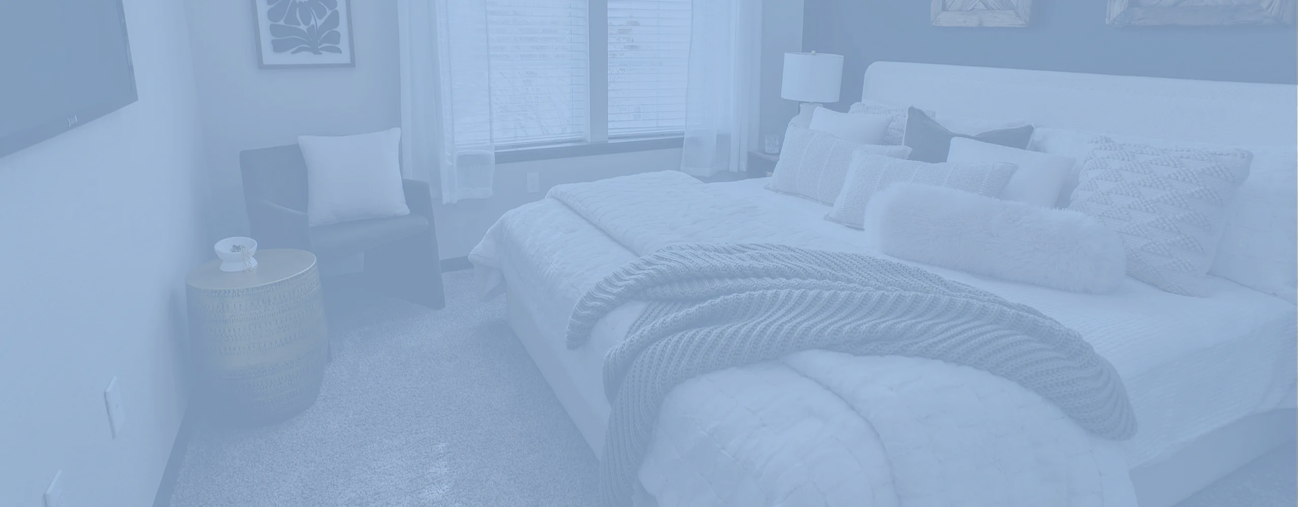 Inviting bedroom with a large cozy bed, plush pillows, and abundant natural light from a large window. Stylish decor enhances a serene and comfortable ambiance.