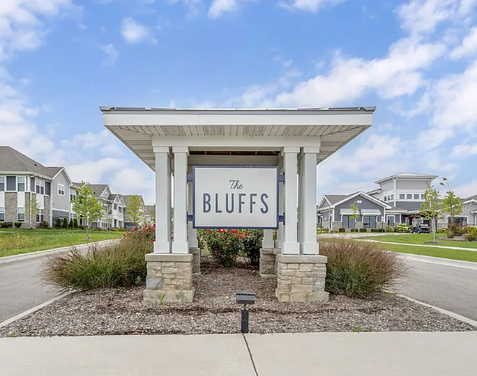 Inviting entrance to The Bluffs community, showcasing beautifully landscaped surroundings and elegant architecture under a bright blue sky.