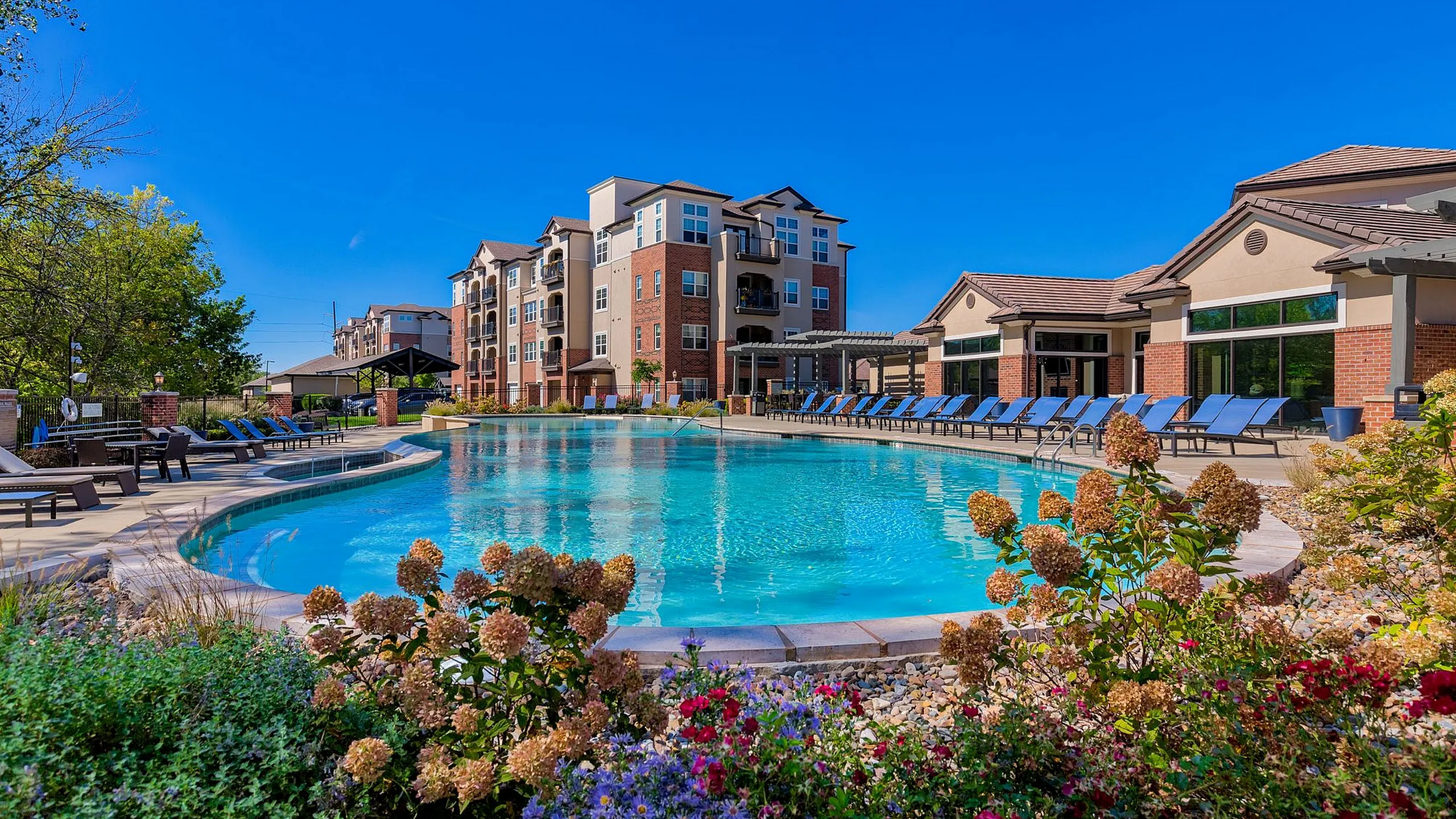 Luxurious apartment complex with sparkling pool, surrounded by lush landscaping and ample sun loungers.