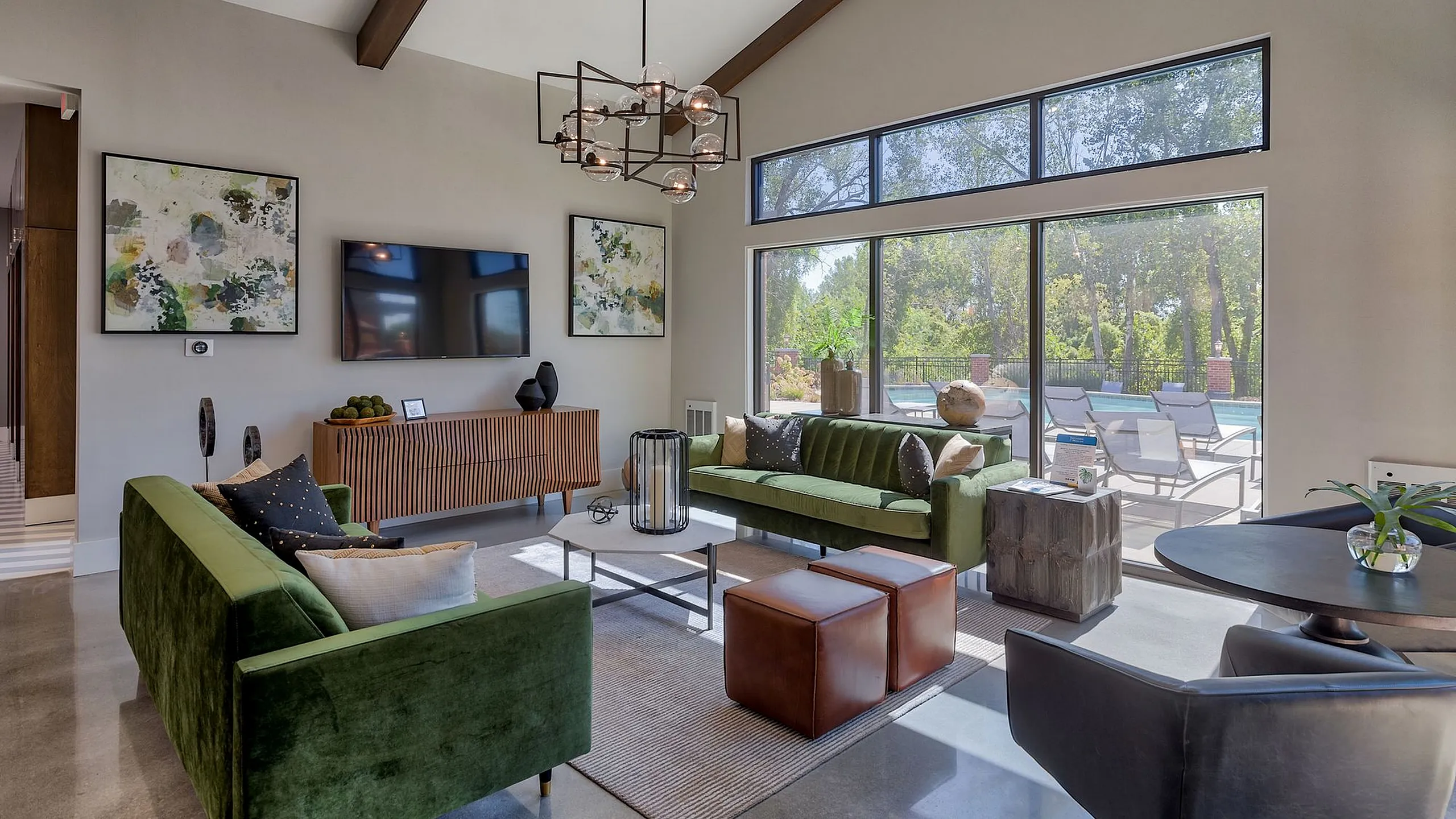 Luxurious living room with modern green sofas, artistic decor, and large windows overlooking a serene poolside view.