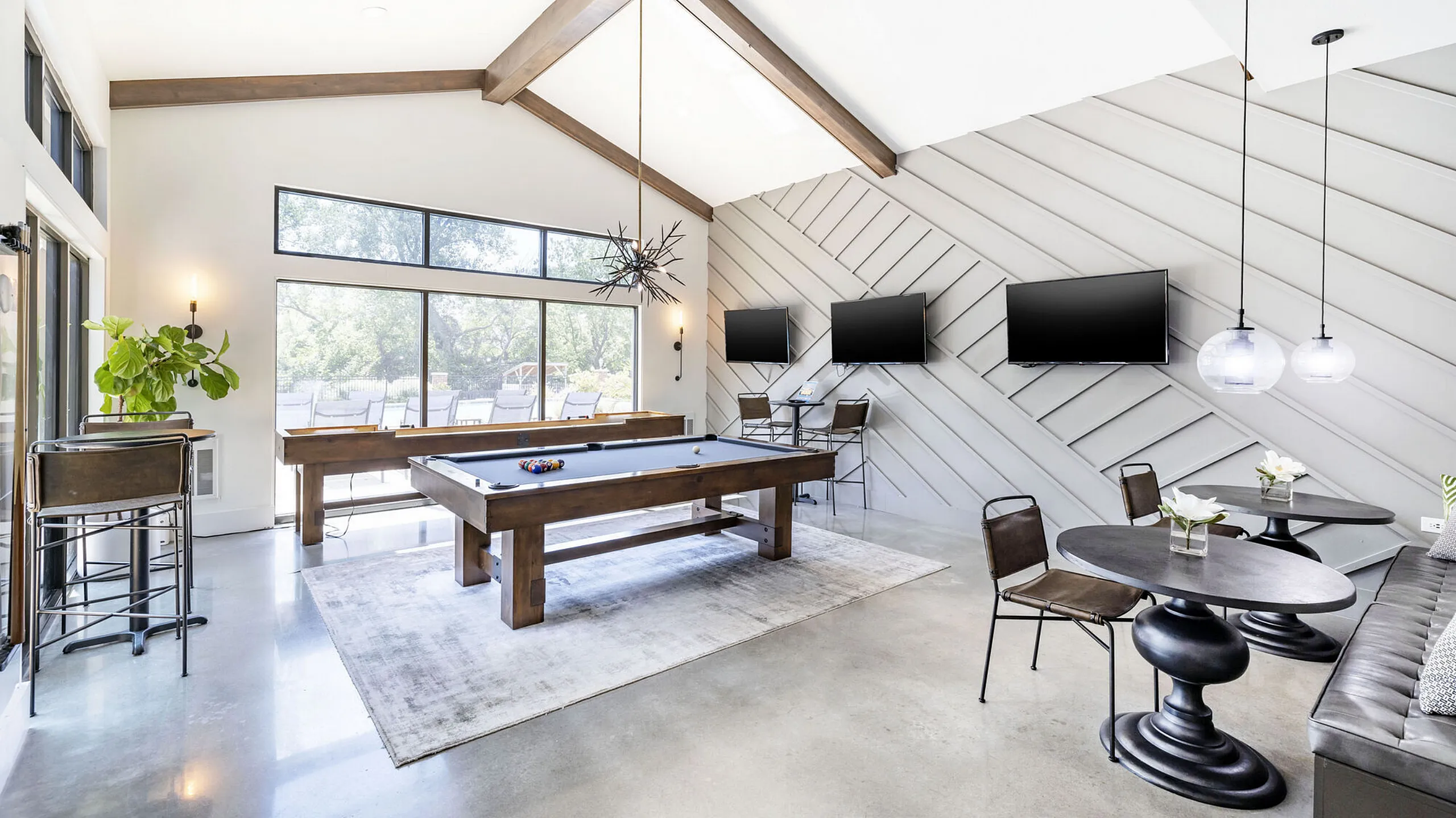 Sleek entertainment room featuring a modern pool table, stylish decor, and large windows overlooking a serene outdoor view.