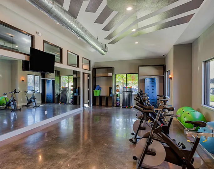 Modern fitness center with stationary bikes, vibrant wall accents, and large mirrors enhancing the open, well-lit space.