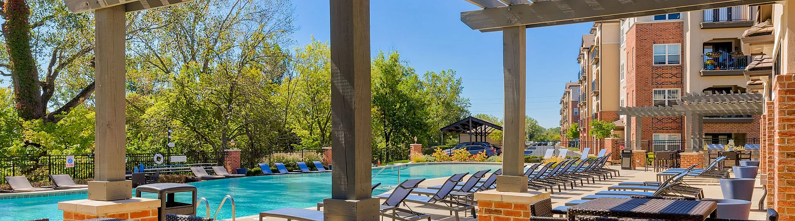 Luxurious apartment complex featuring a stunning outdoor pool area with modern lounge chairs and lush greenery.