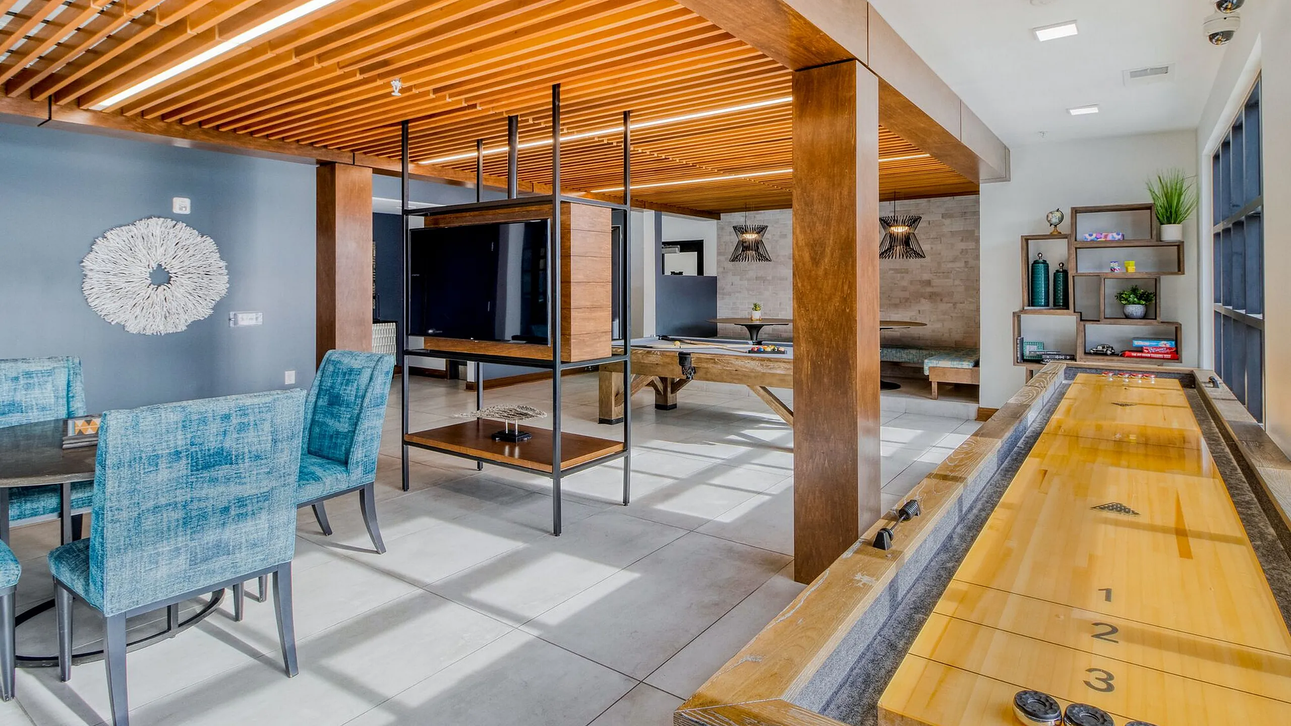 Inviting and modern recreation room featuring stylish blue chairs, wooden accents, and a shuffleboard table, perfect for entertainment and relaxation.