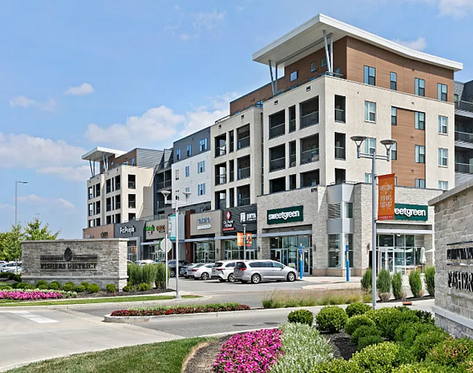 Modern mixed-use building with retail shops and stylish residential apartments, surrounded by vibrant landscaping in a lively district.