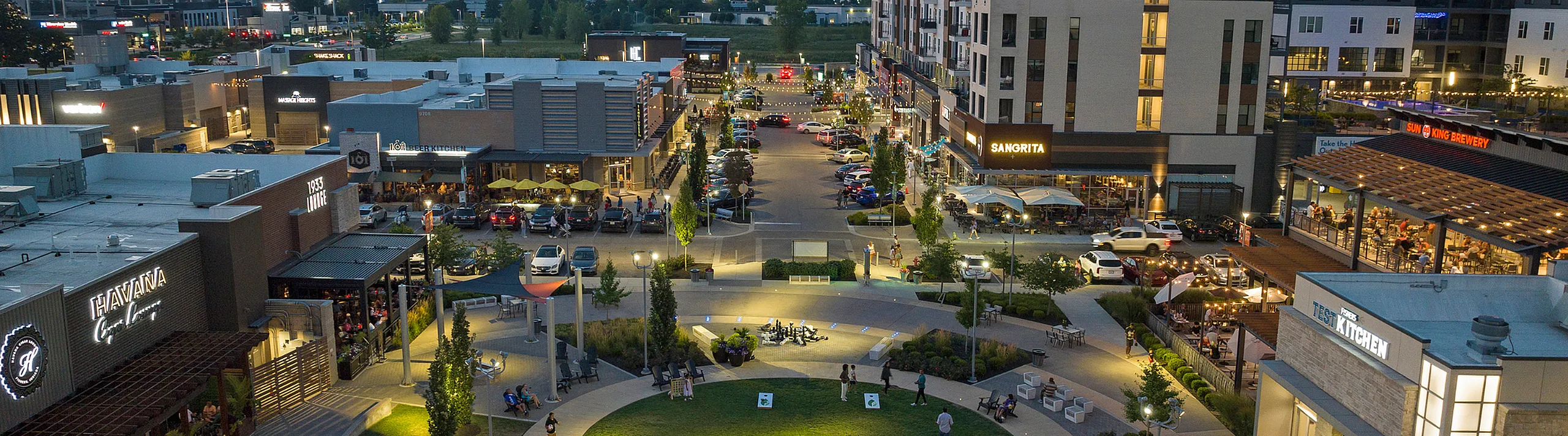 Vibrant evening view of a lively urban shopping district with illuminated restaurants, bustling streets, and modern architecture.