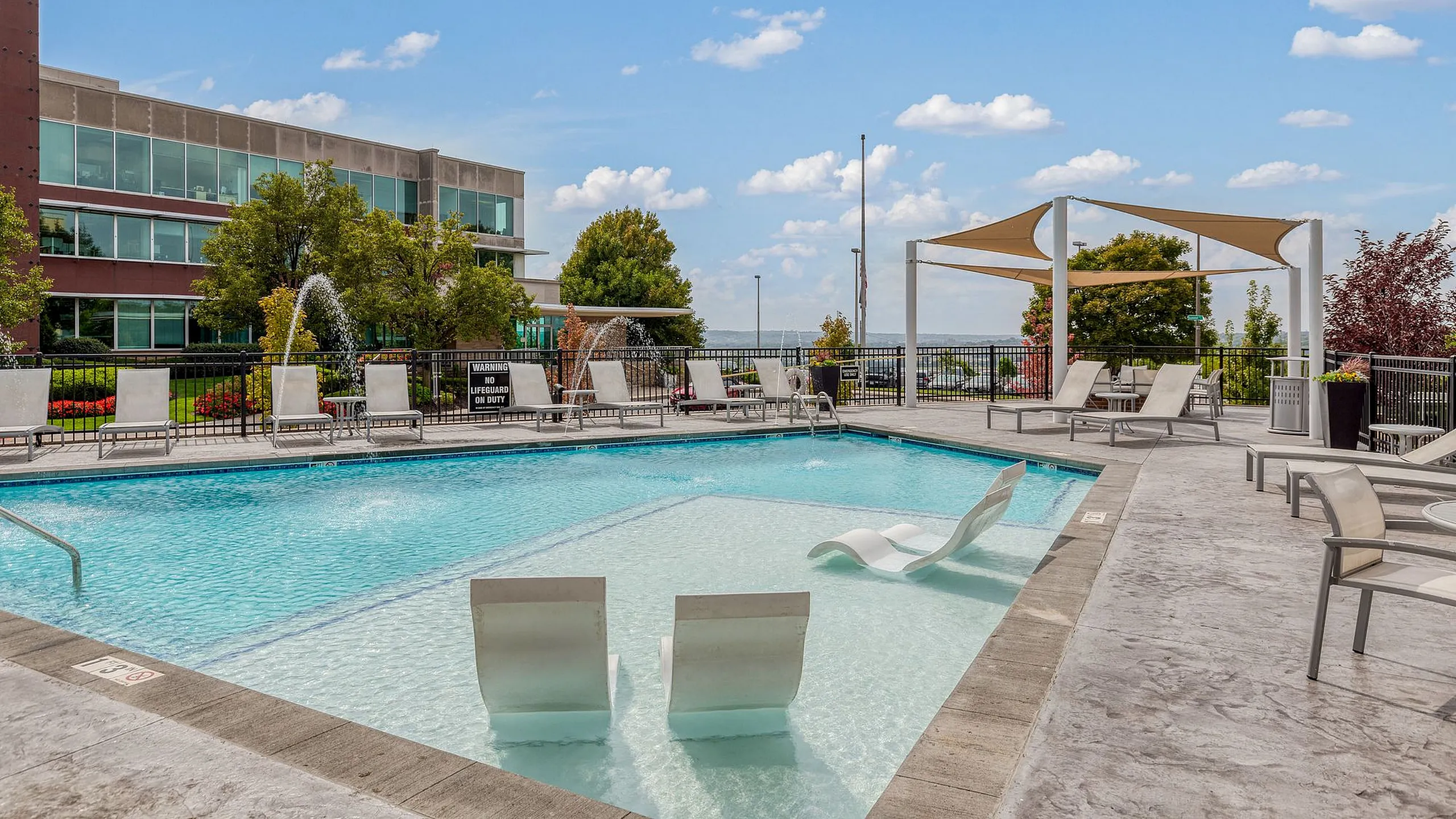 Luxurious apartment complex showcasing a sparkling outdoor pool with chic lounge chairs, surrounded by lush greenery and modern architecture.