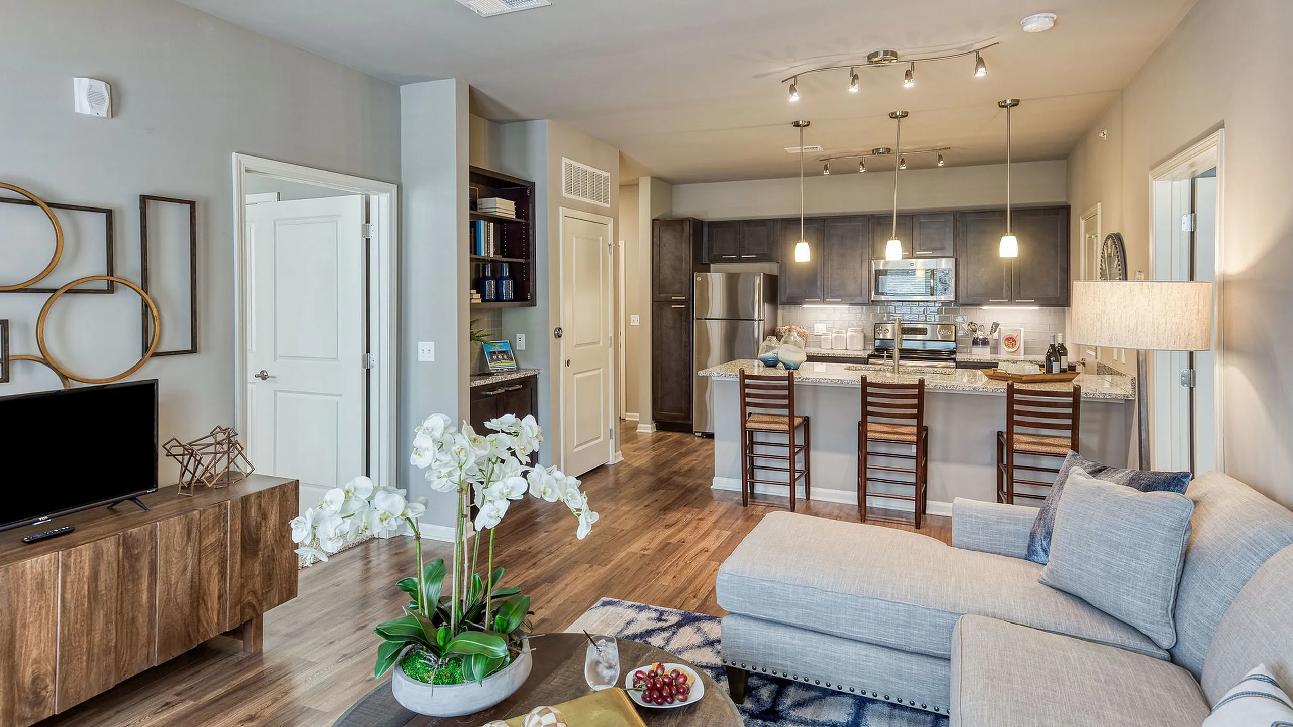 Modern living area featuring a cozy open-plan space with elegant decor, stylish kitchen island with pendant lights, and chic wooden flooring.