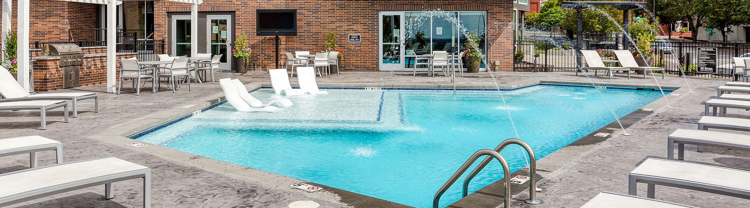 Luxurious apartment complex featuring a sparkling pool with sun loungers and a BBQ area, perfect for relaxation and entertaining.