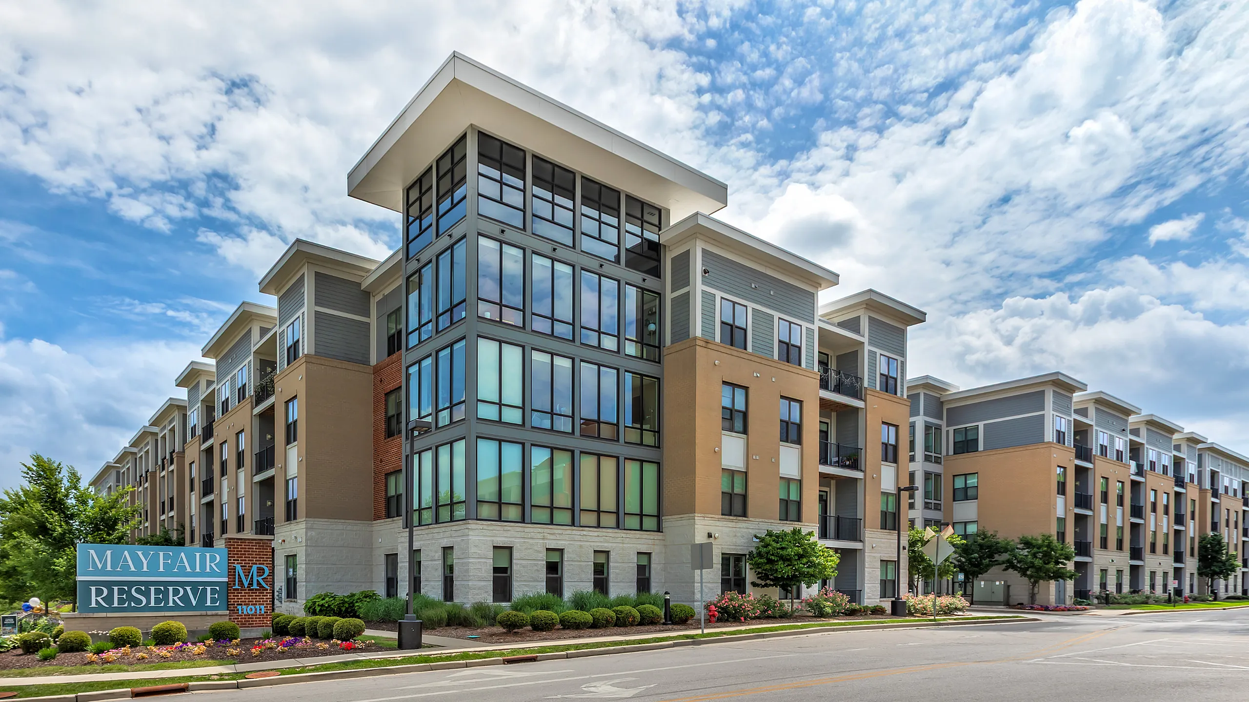 Contemporary Mayfair Reserve apartment complex with large windows and manicured landscaping under a vibrant blue sky.