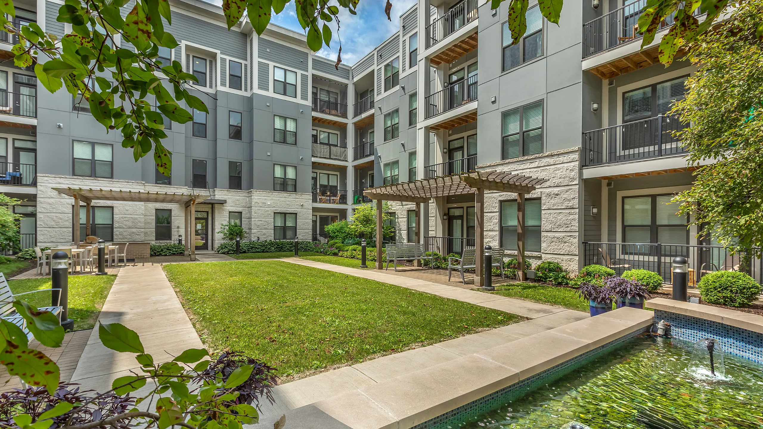 Beautiful apartment complex with modern architecture, lush greenery, and a tranquil courtyard fountain.