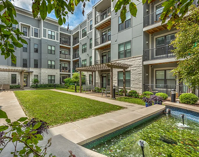 Charming courtyard view of a modern apartment complex with lush greenery, a tranquil fountain, and elegant balconies.