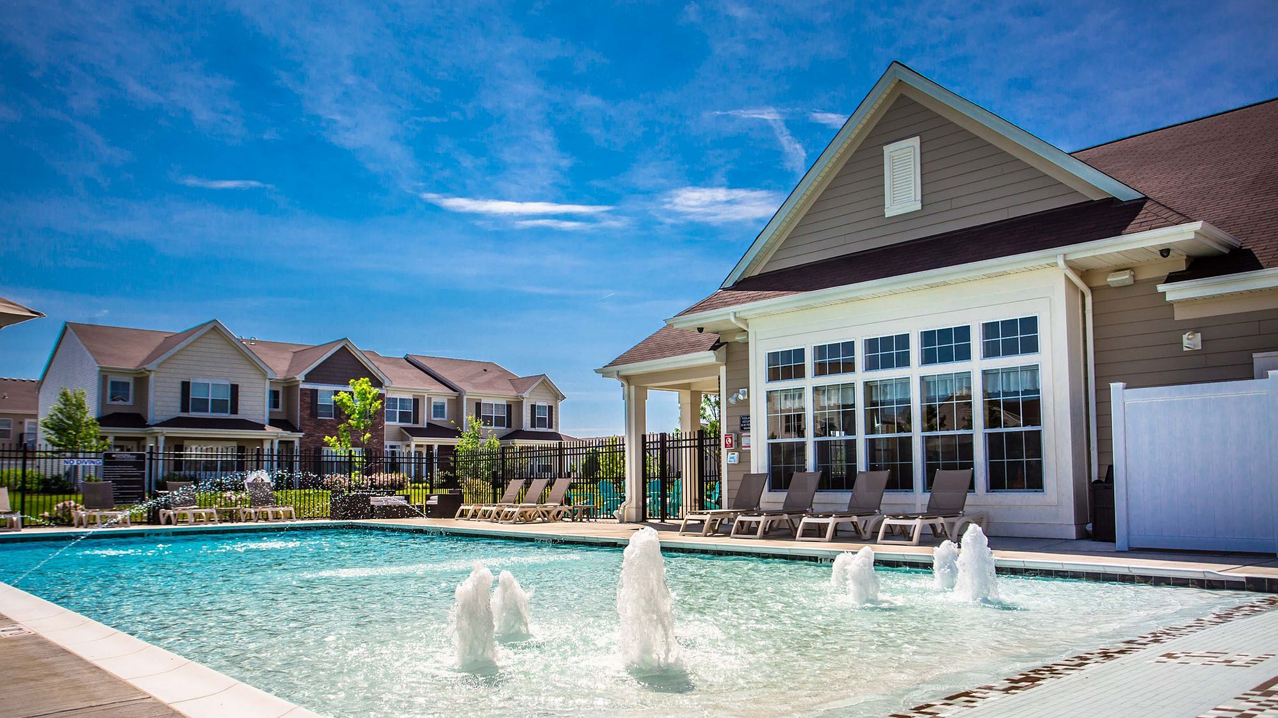 Inviting apartment complex with luxurious poolside loungers, pristine swimming pool and picturesque community setting.