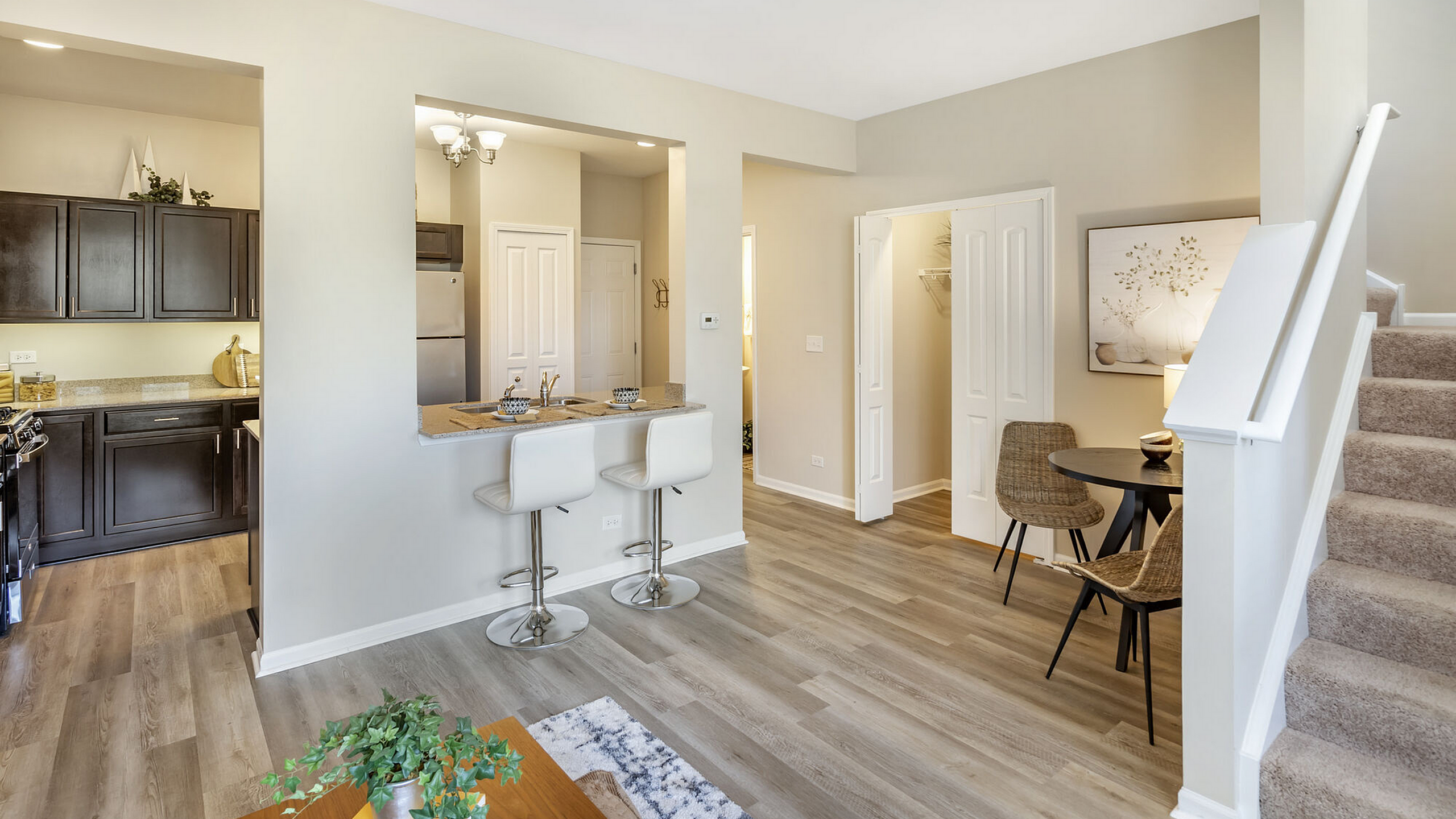Modern apartment interior with open kitchen, cozy breakfast bar, and elegant dining area beside carpeted stairs.