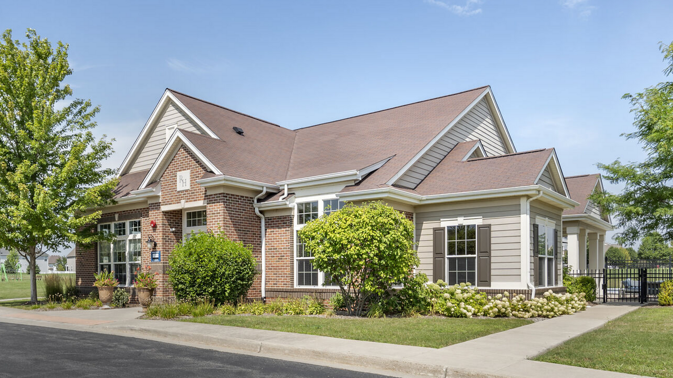 Charming single-story house with brick and siding exterior, surrounded by lush greenery and a well-maintained landscape, offering a serene suburban feel.