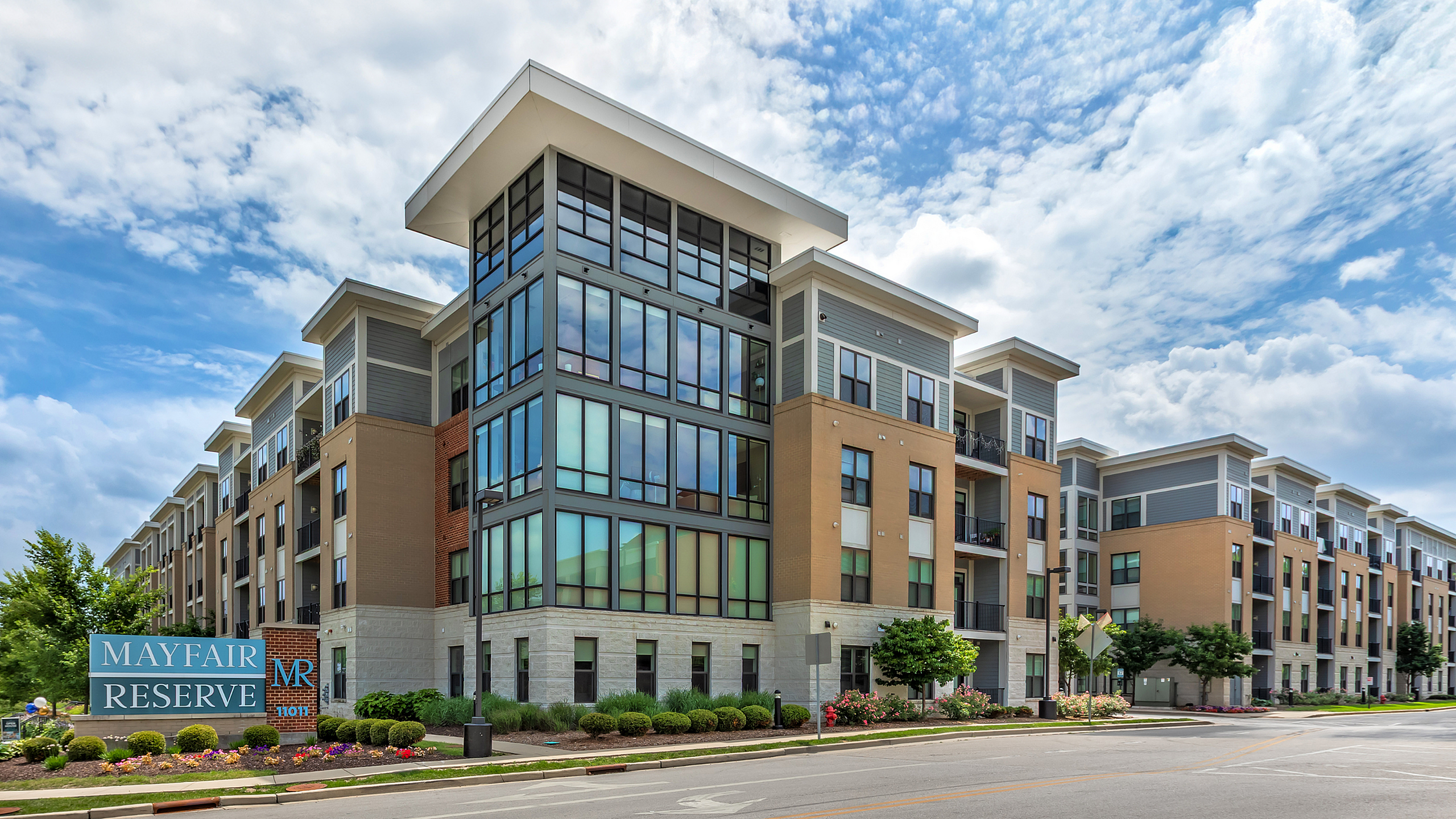 Contemporary Mayfair Reserve apartment complex with large windows and manicured landscaping under a vibrant blue sky.