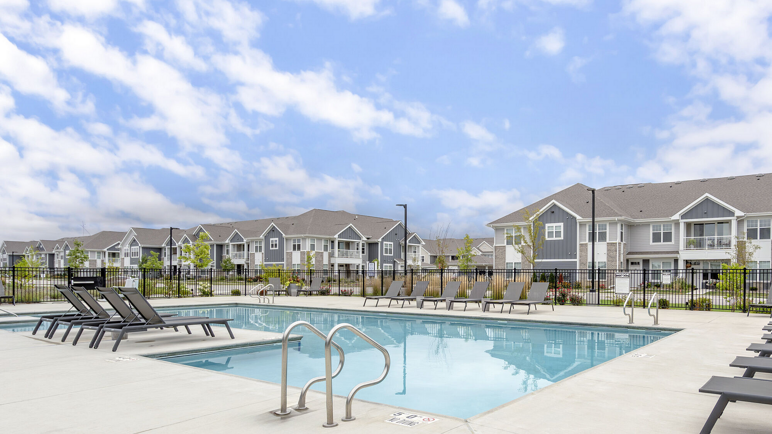 Charming apartment complex with modern architecture and a sparkling pool, set under a clear blue sky.
