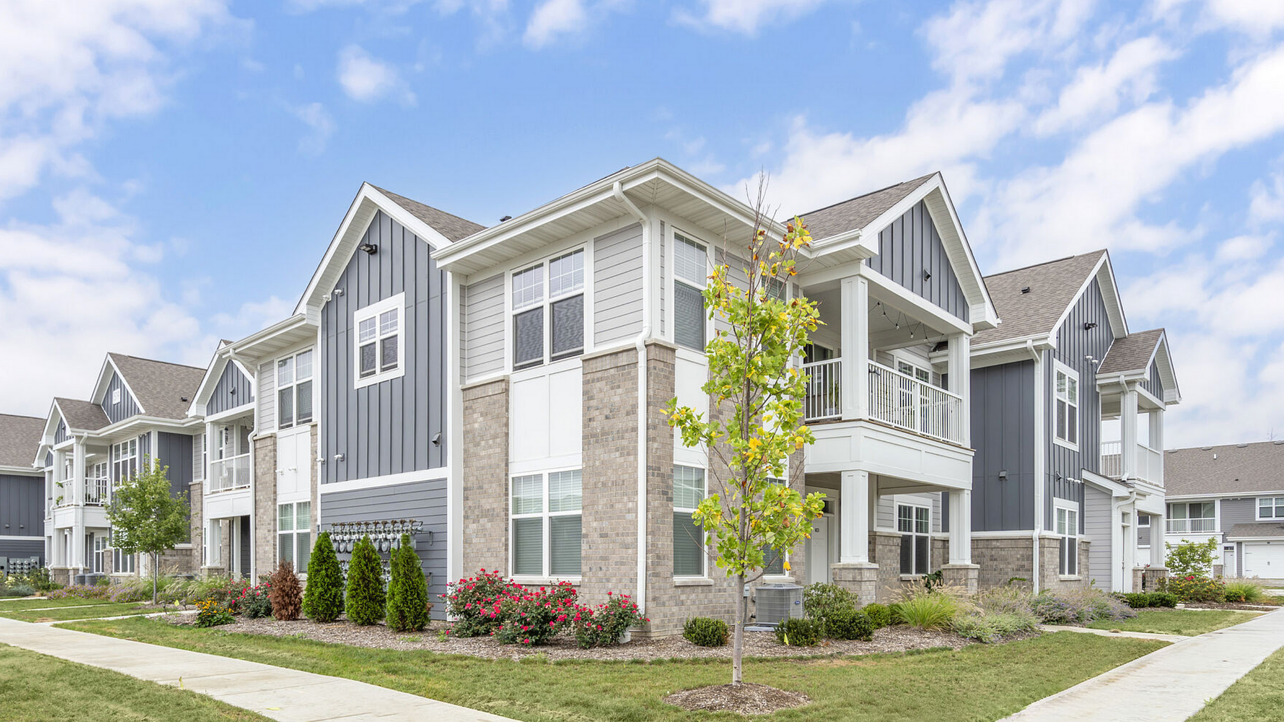 Charming modern apartment complex featuring stylish blue-gray panels, elegant architecture, well-maintained landscaping, and inviting balconies.