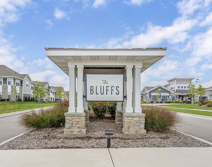 Inviting entrance to The Bluffs community, showcasing beautifully landscaped surroundings and elegant architecture under a bright blue sky.